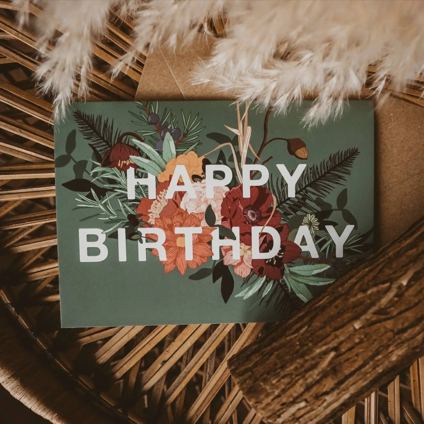 Floral 'Happy Birthday' card on a woven surface with pampas grass