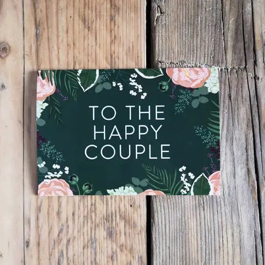 Card with 'To the Happy Couple' text on a floral design, placed on wooden surface