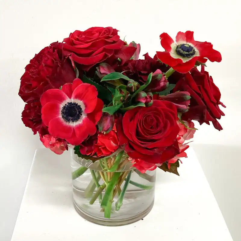 Bouquet of red roses and anemones in a clear vase on a white background
