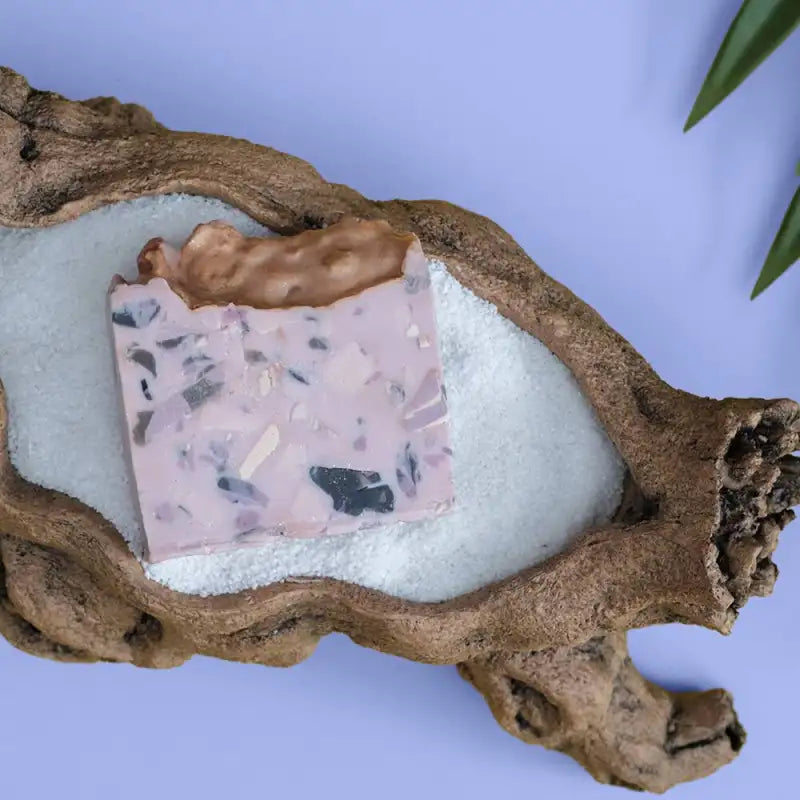 Bar of soap with a terrazzo pattern in a natural wood holder on a light blue background