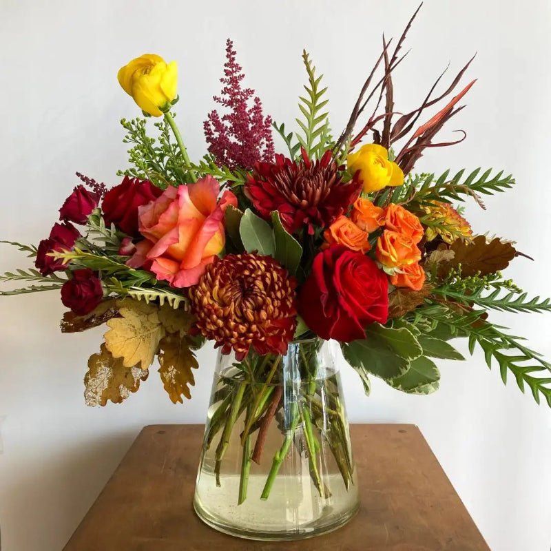 Bouquet of flowers in a clear vase on a wooden surface with a white background
