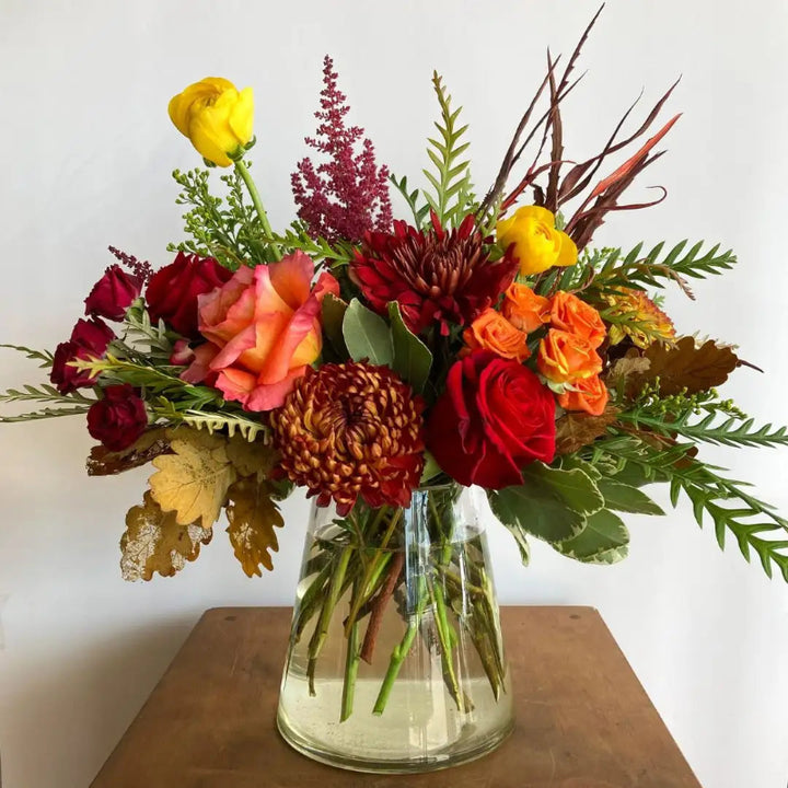 Bouquet of flowers in a clear vase on a wooden surface with a white background