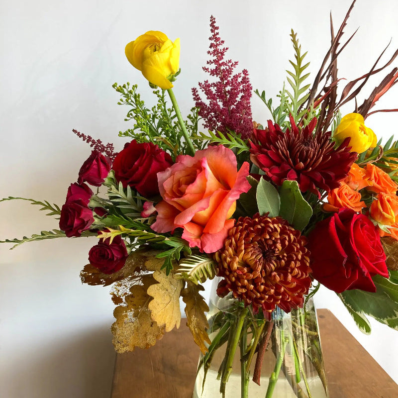 Colorful flower arrangement in a glass vase on a wooden surface with a white background