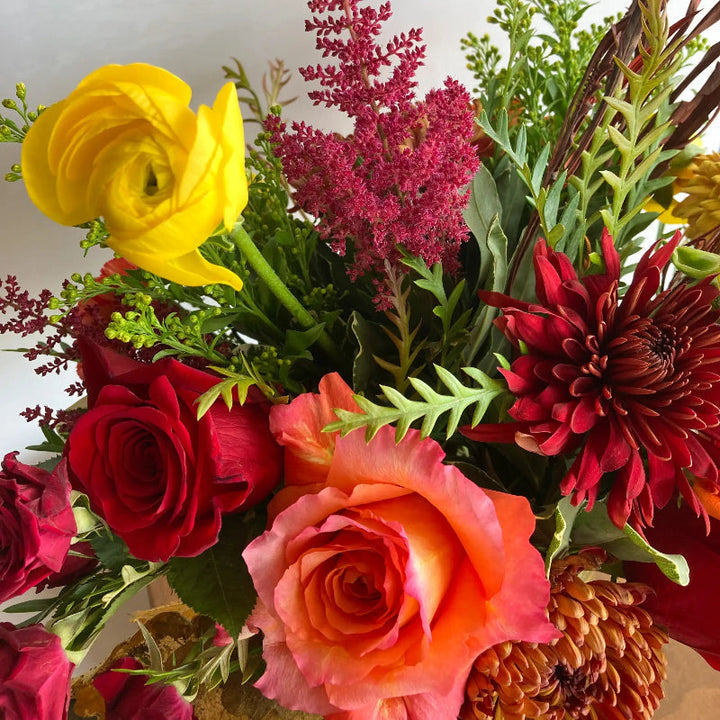 Bouquet of colorful flowers including red roses, yellow ranunculus, and pink astilbe.