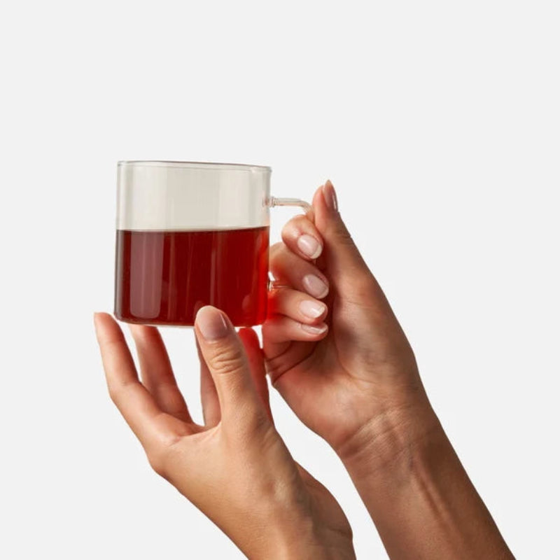 Two hands holding a glass mug with red liquid against a white background