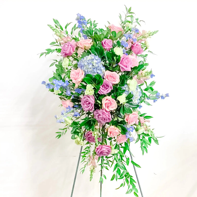 Floral arrangement with pink, blue, and green flowers on a stand against a white background