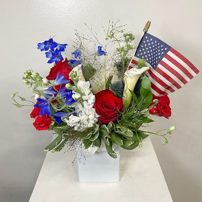 Patriotic red, white, and blue flower arrangement for 4th of July celebrations with fresh seasonal flowers in a white container.