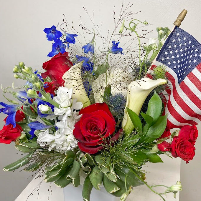 Patriotic red, white, and blue flower arrangement for 4th of July celebrations with fresh seasonal flowers in a white container.