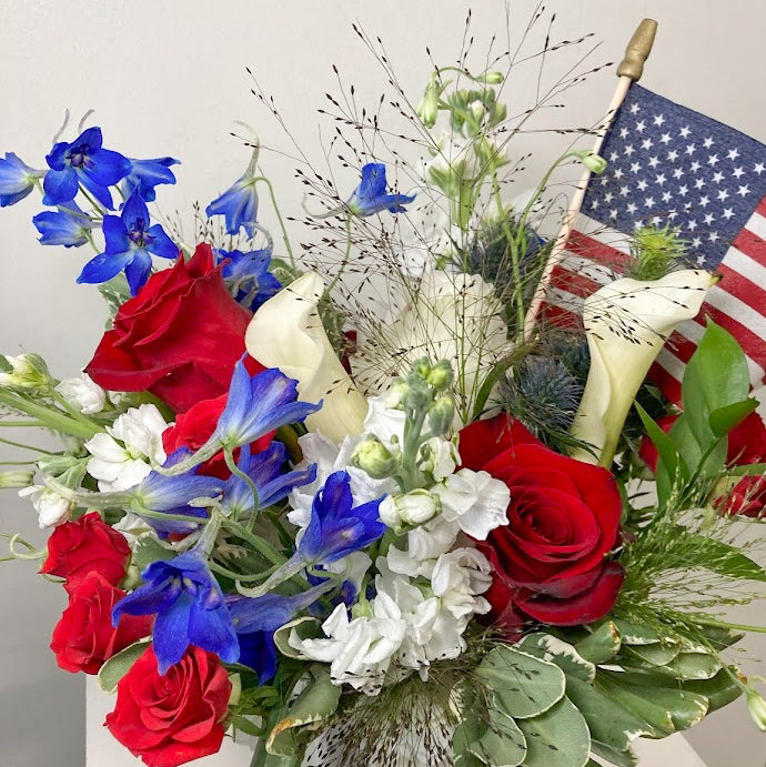 Patriotic red, white, and blue flower arrangement for 4th of July celebrations with fresh seasonal flowers in a white container.