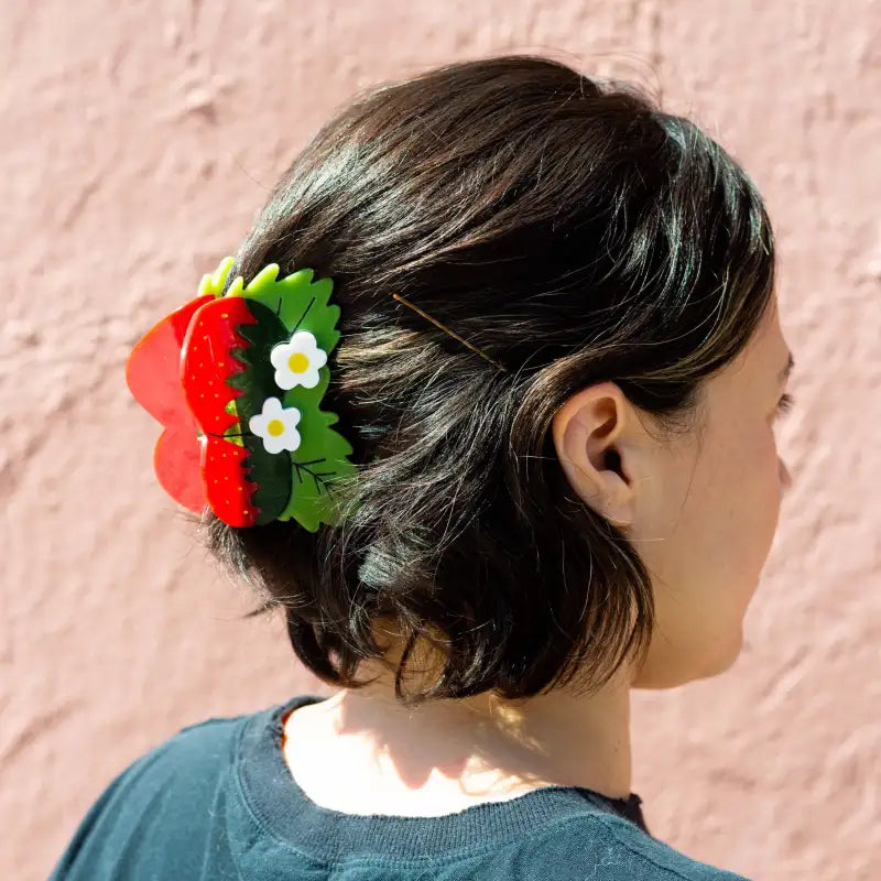 Person with a decorative hair claw shaped like a strawberry and flower against a pink background