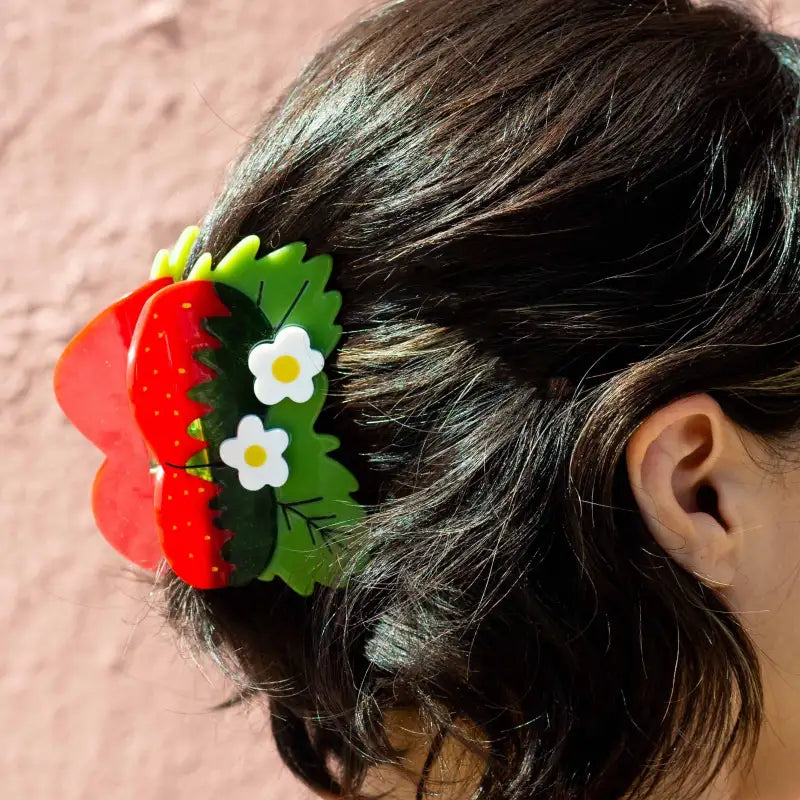 Hair claw with strawberry and flower design on a person's hair against a pink background