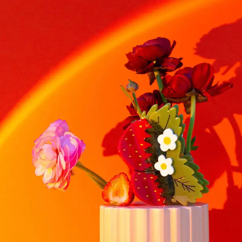 Decorative flowers and strawberry hair claw on a stand against a red and orange gradient background