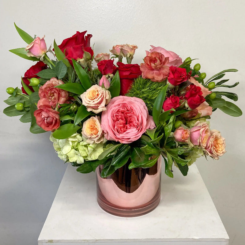 Bouquet of red, pink, and green flowers in a pink vase on a white surface.