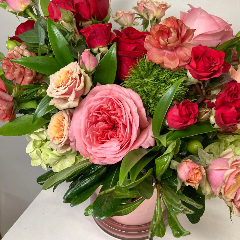 Bouquet of colorful flowers including pink, red, and green in a pink vase.