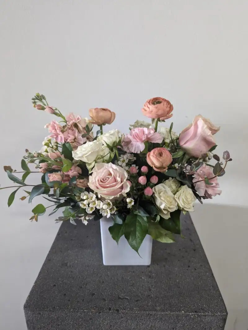 Bouquet of pink and white flowers in a white vase on a gray surface with a light gray background