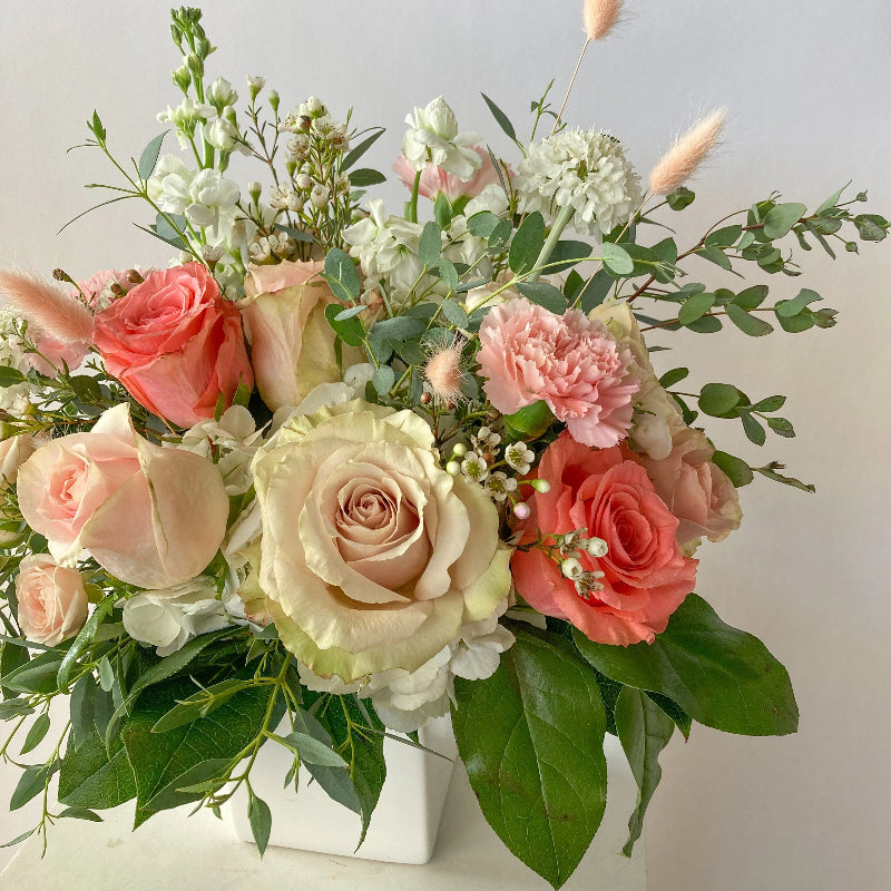 Bouquet of pink and white flowers with greenery in a white container on a light gray background