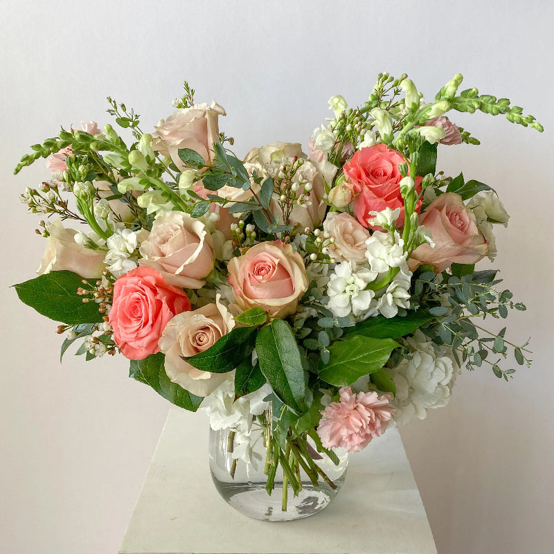 Bouquet of pink, white, and green flowers in a clear vase on a light surface with a light gray background