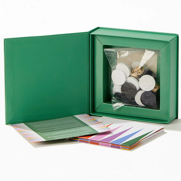 Green box with a clear window containing small round objects, on a white background