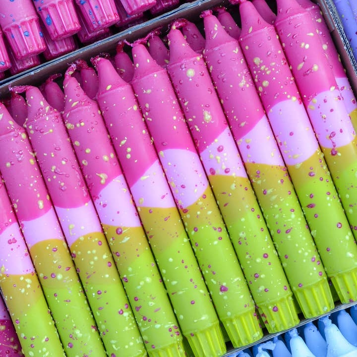 A close-up of taper candles in a tray, featuring a repeating pattern of pink, light pink, and bright lime green sections with small confetti speckles.