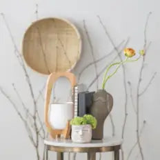 Decorative setup with a round mirror, potted plants, and body vases on a white surface.