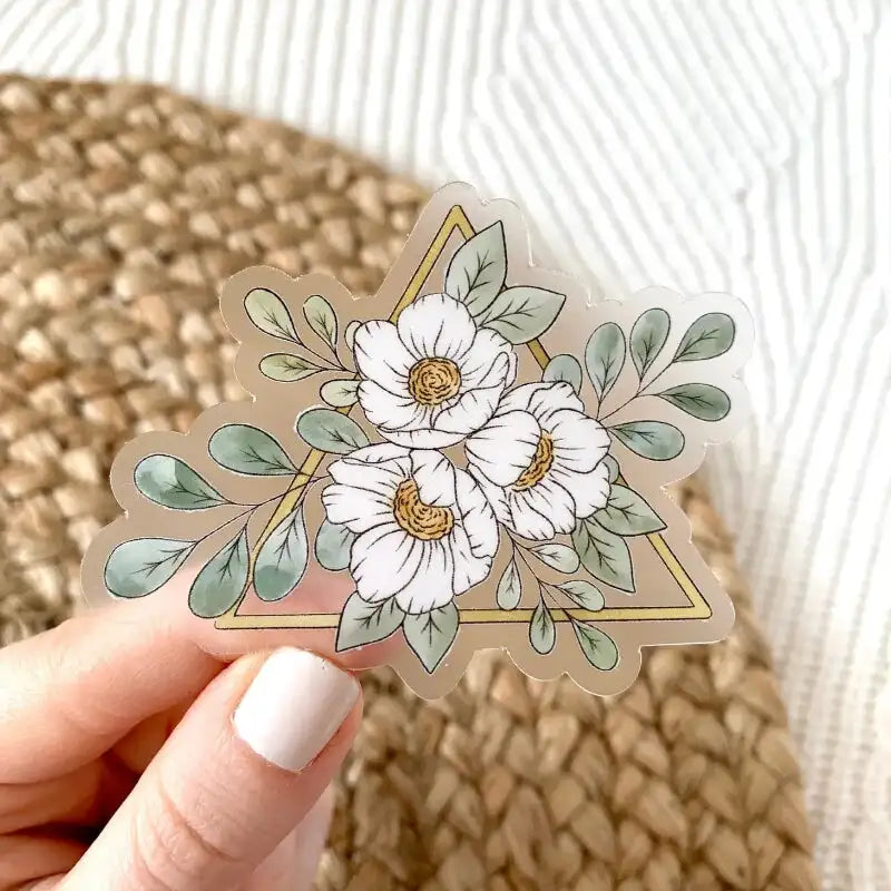Hand holding a clear vinyl sticker with white floral design on a textured surface
