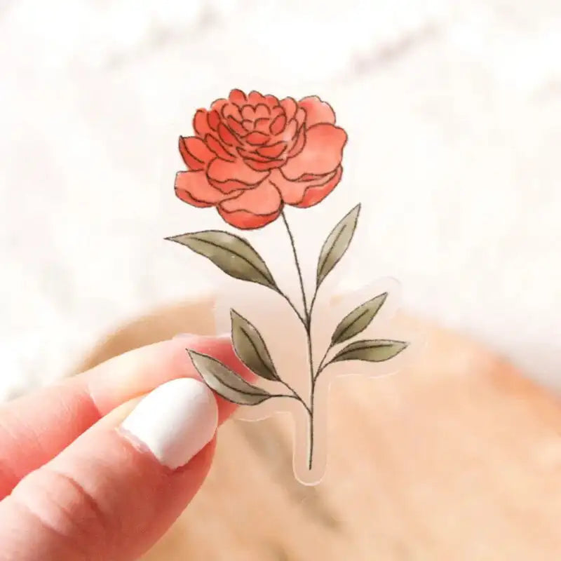 Hand holding a clear acrylic sticker with a red flower design on a light background