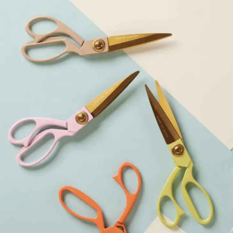 Four pairs of scissors with different colored handles on a light blue and beige background.