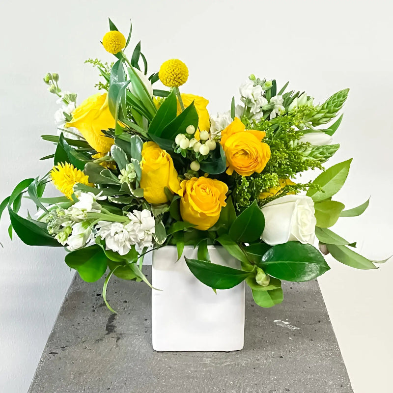 Bouquet of yellow and white flowers in a white vase on a gray surface with a light gray background