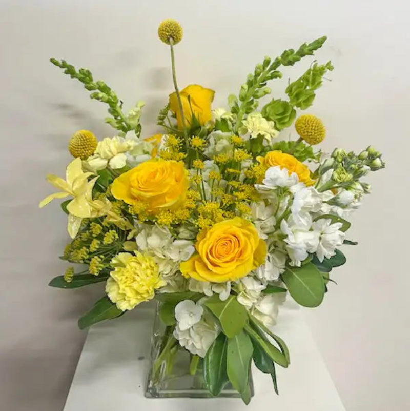 Bouquet of yellow and white flowers in a clear vase on a light background