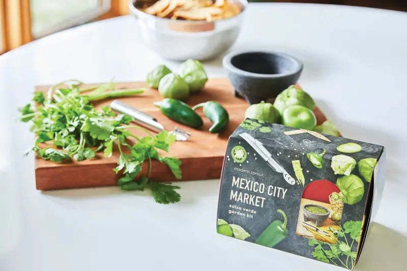 Garden kit packaging labeled 'Mexico City Market' on a table with vegetables and a cutting board.