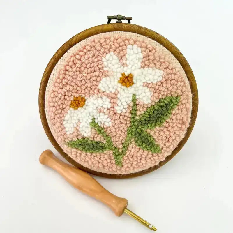 Floral punch needle art with a wooden tool on a white background
