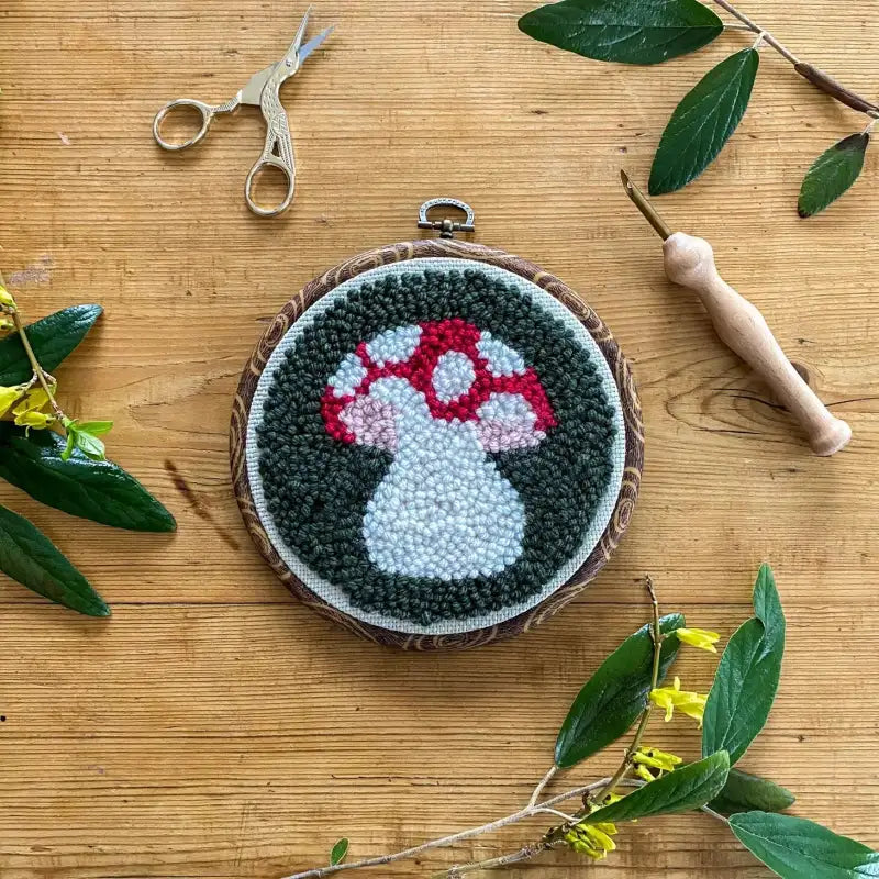 Embroidery hoop with mushroom design on a wooden surface with scissors and leaves.