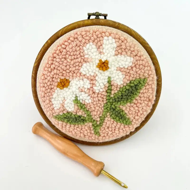 Embroidery hoop with floral design and wooden needle on a white background