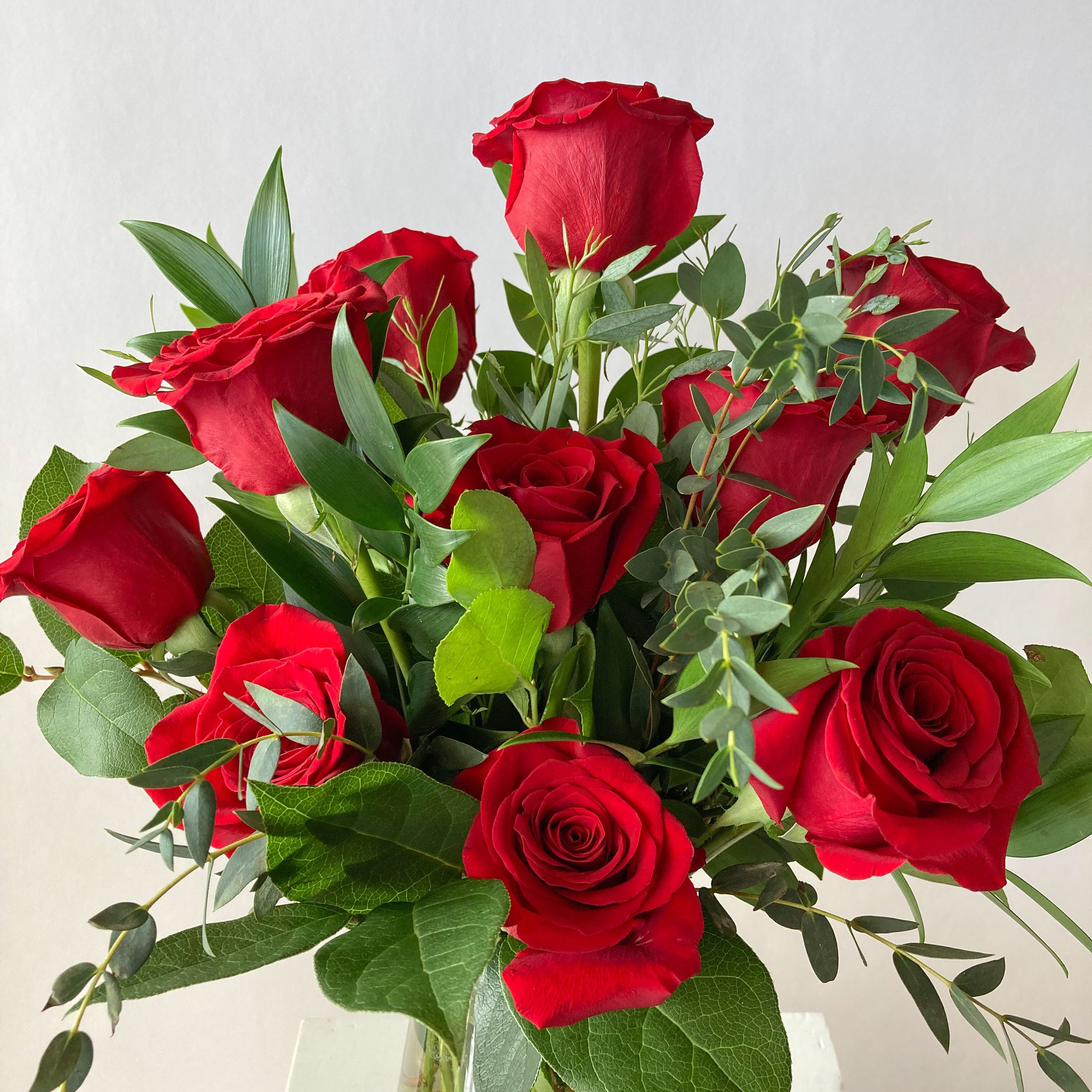 Bouquet of red roses with green leaves in a clear vase on a light background