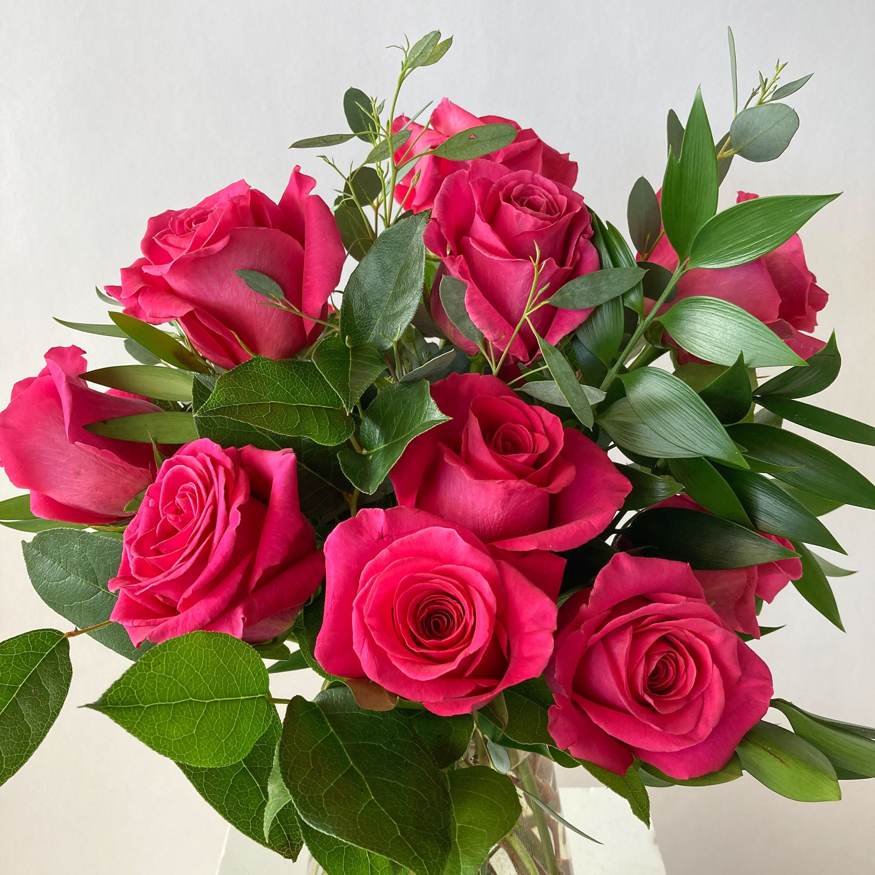 Bouquet of bright pink roses with green leaves in a clear vase on a light background