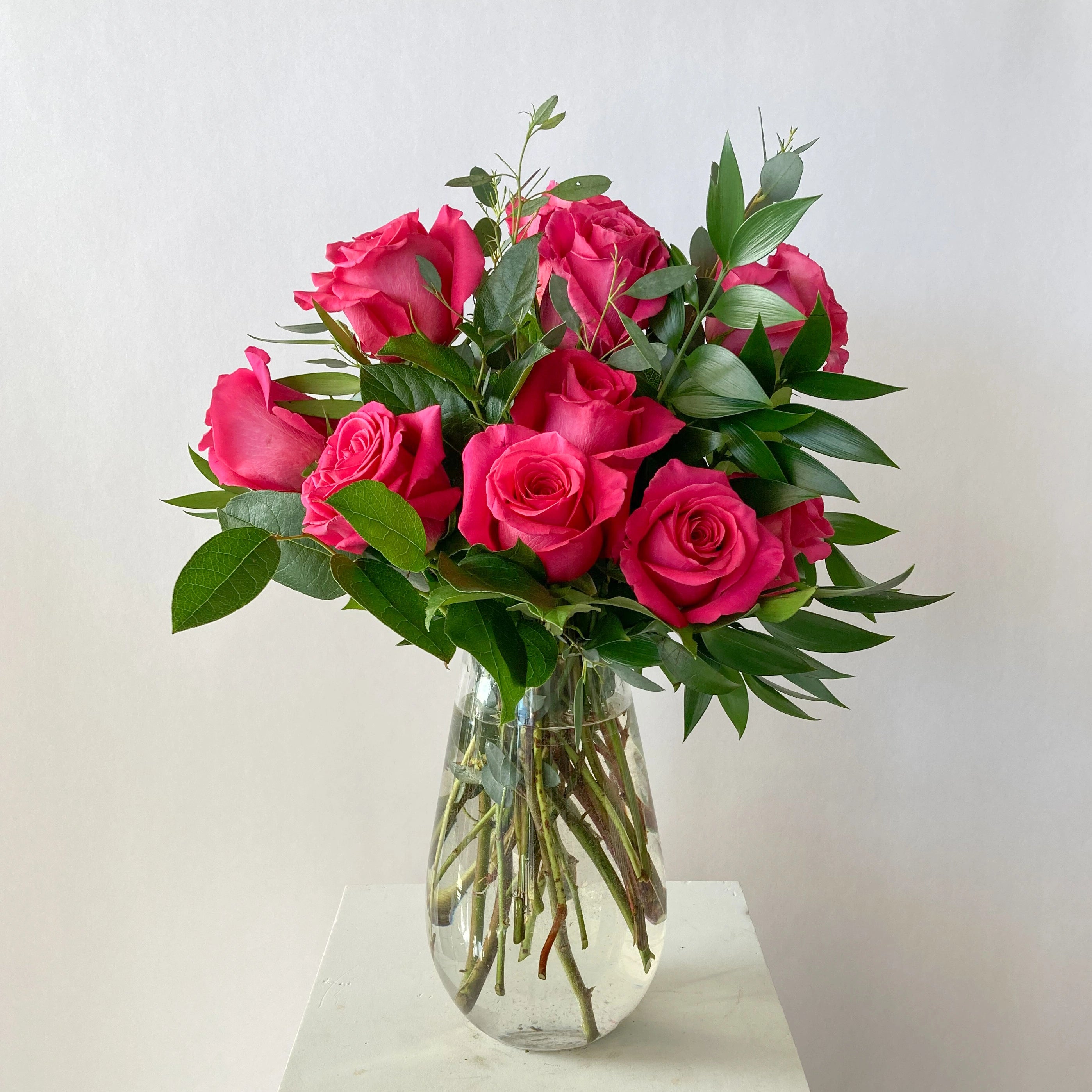 Bouquet of pink roses in a clear vase on a white surface with a light gray background