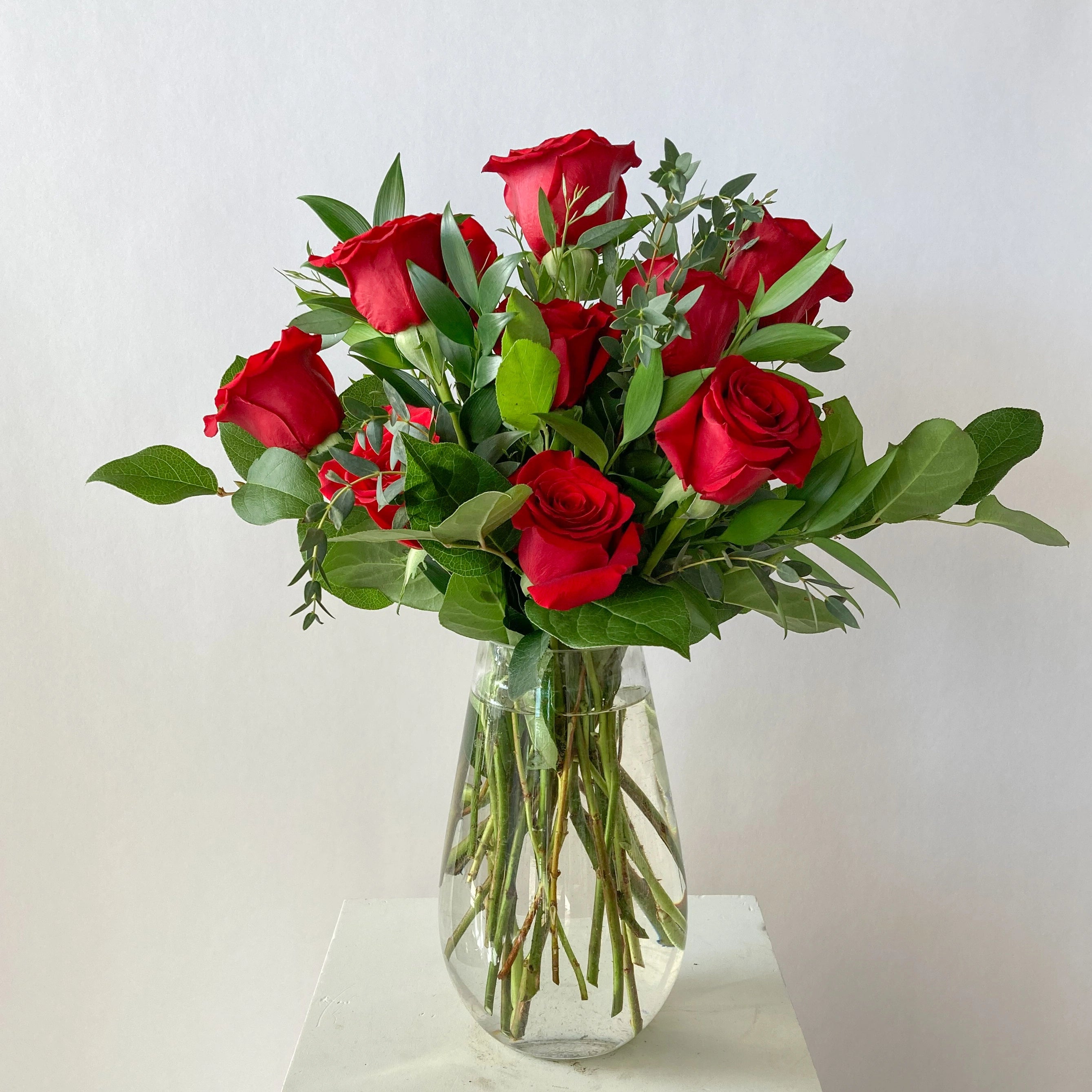 Bouquet of red roses in a clear vase on a white surface with a light gray background