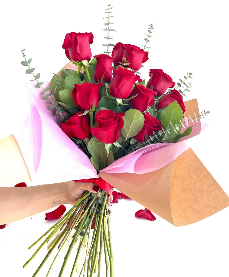 Bouquet of red roses being wrapped with pink paper and brown tape on a white background