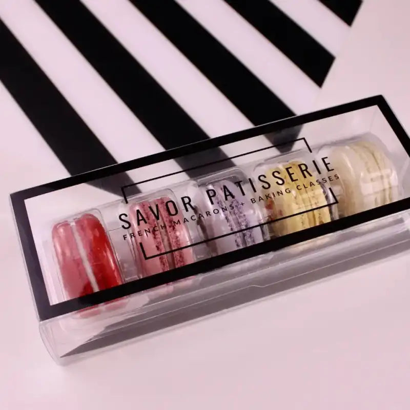 Set of Savor Patisserie macarons in a clear box on a black and white striped background