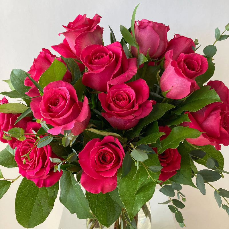 Bouquet of bright pink roses in a clear vase on a light background
