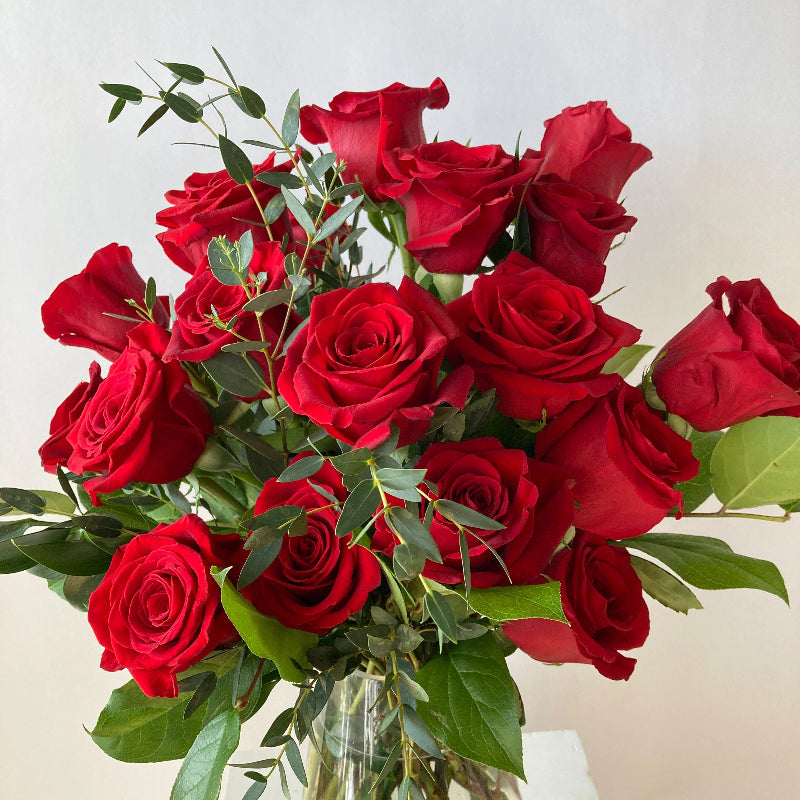 Bouquet of red roses in a clear vase on a light background