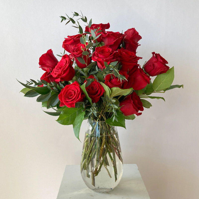 Bouquet of red roses in a clear vase on a light background