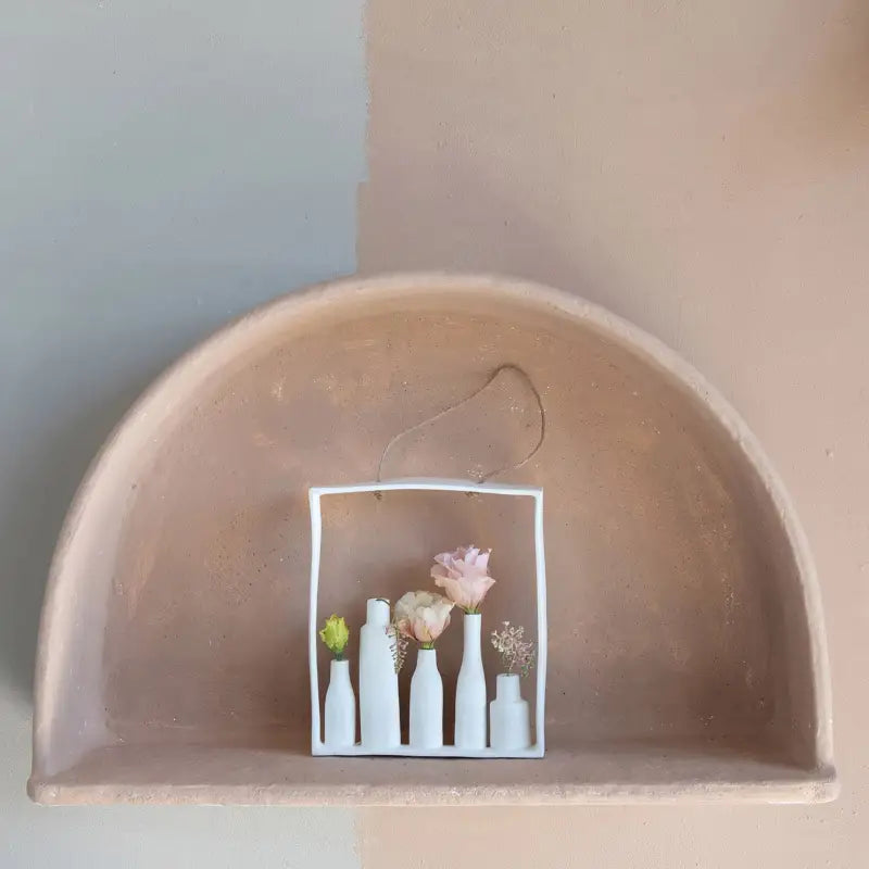 Decorative shelf with a small square mirror reflecting bottles and flowers.