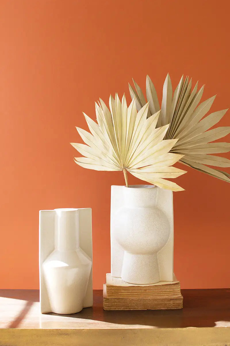 Two white vases with a dried plant against an orange wall