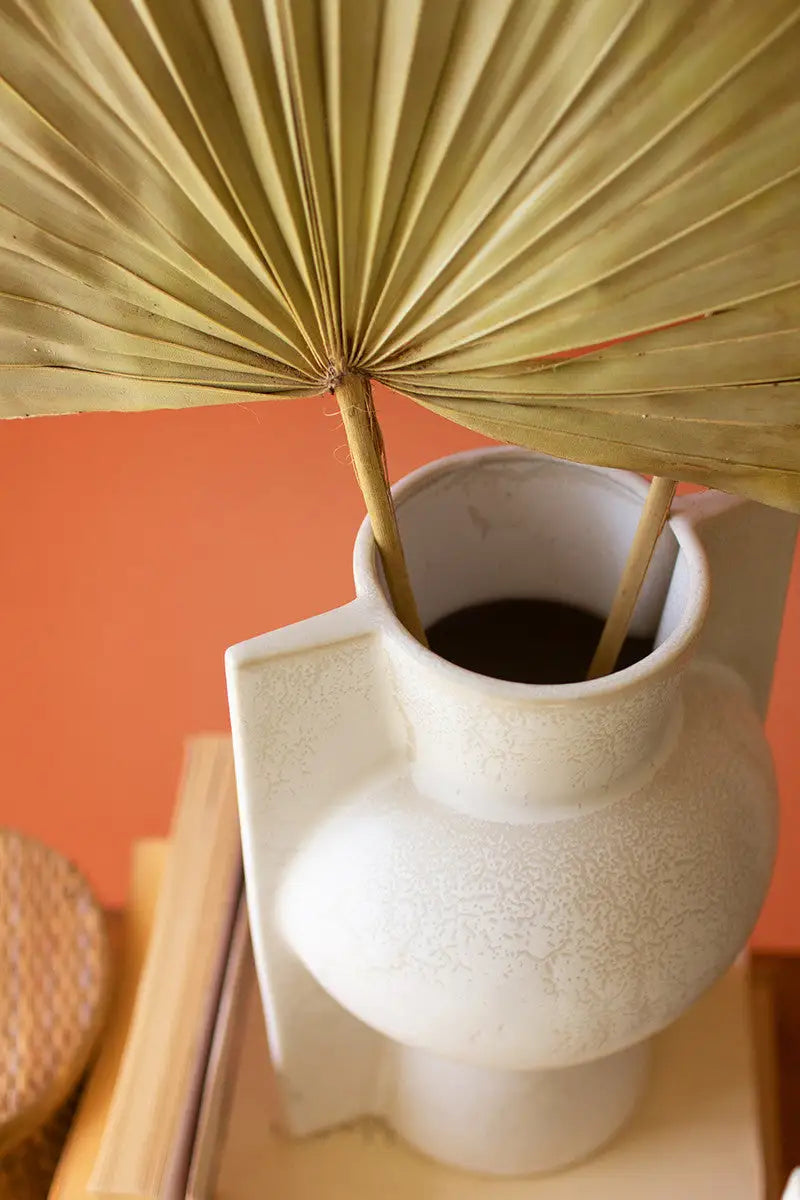 White textured vase with dried palm leaves against an orange wall