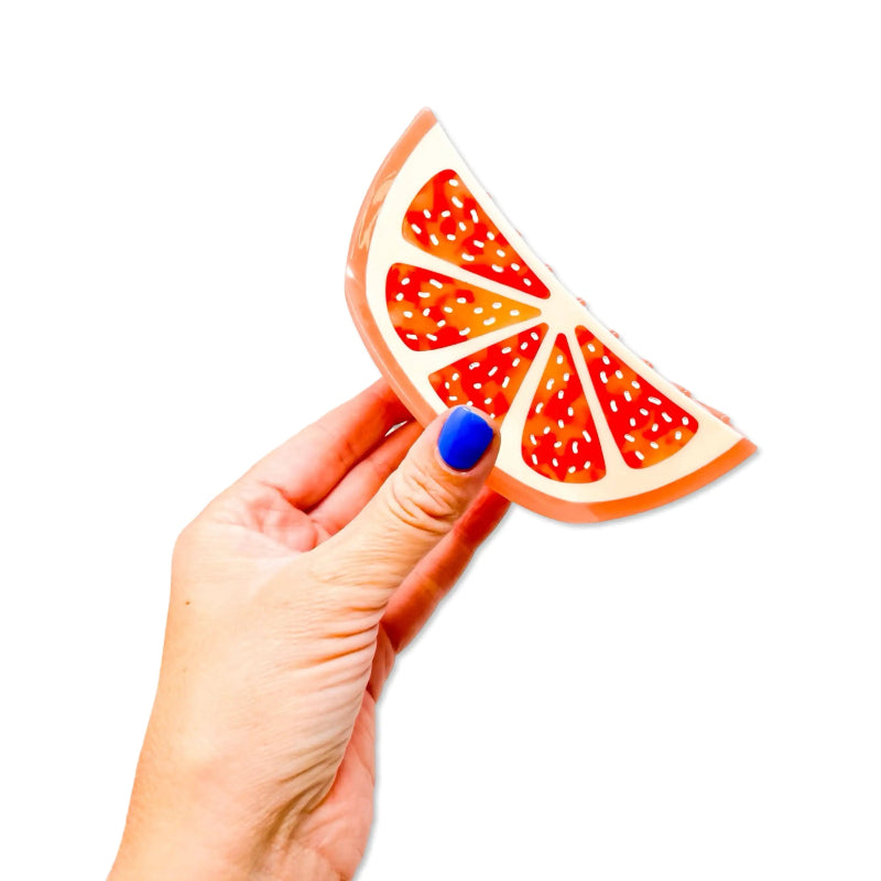 Hand holding a grapefruit slice-shaped object against a white background