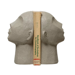 A pair of beige resin bookends shaped like human heads, with a novel placed horizontally on one of the bookends.