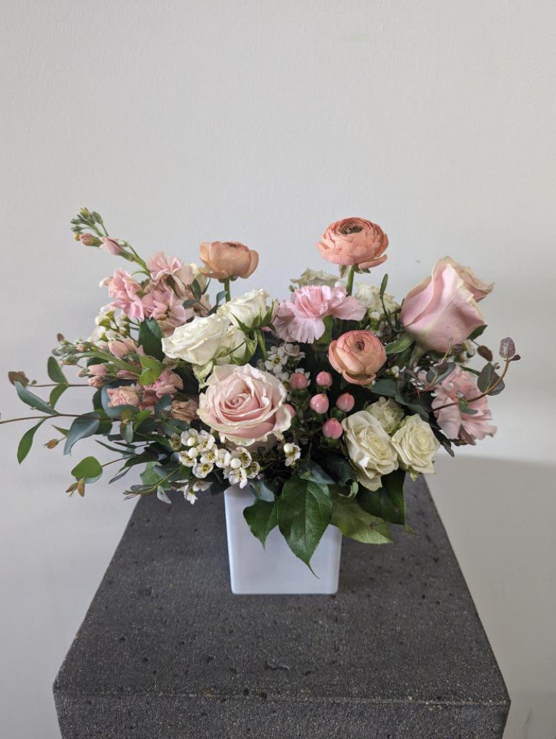 Elegant pink and peach flower arrangement with roses and ranunculus in a white vase for delivery