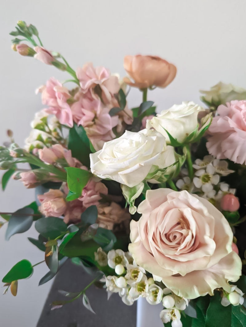Close-up of pink and white floral bouquet with roses, ranunculus, wax flowers, and greenery in a modern white vase for flower delivery